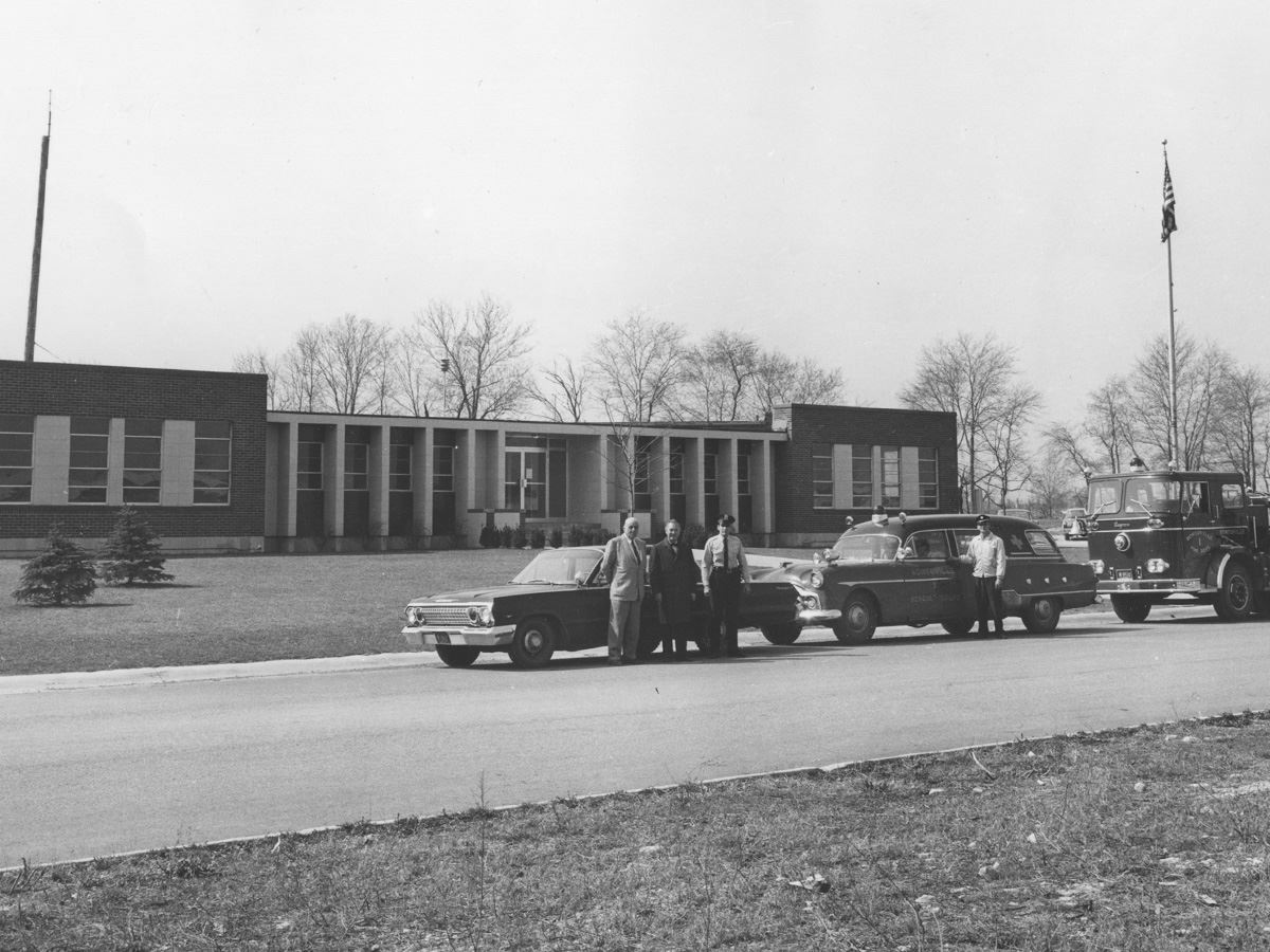 Mayor Murphy and others stand in front of Village Hall with police and fire vehicle.